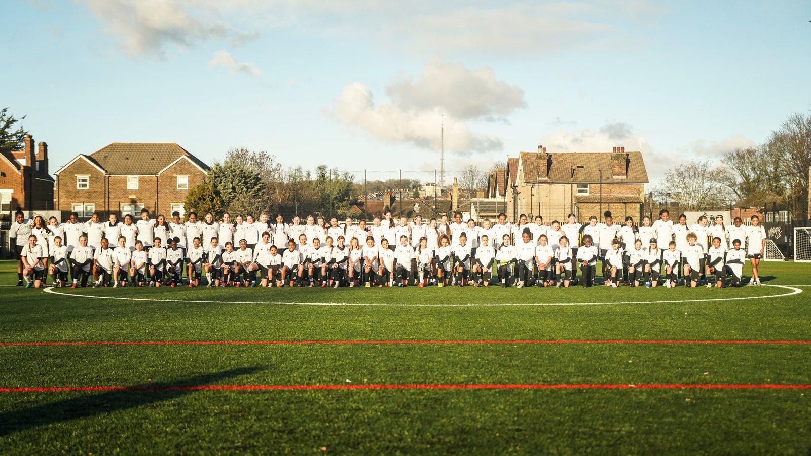More than a hundred girls in Monster Mentality and adidas kit lined up across a pitch in South London