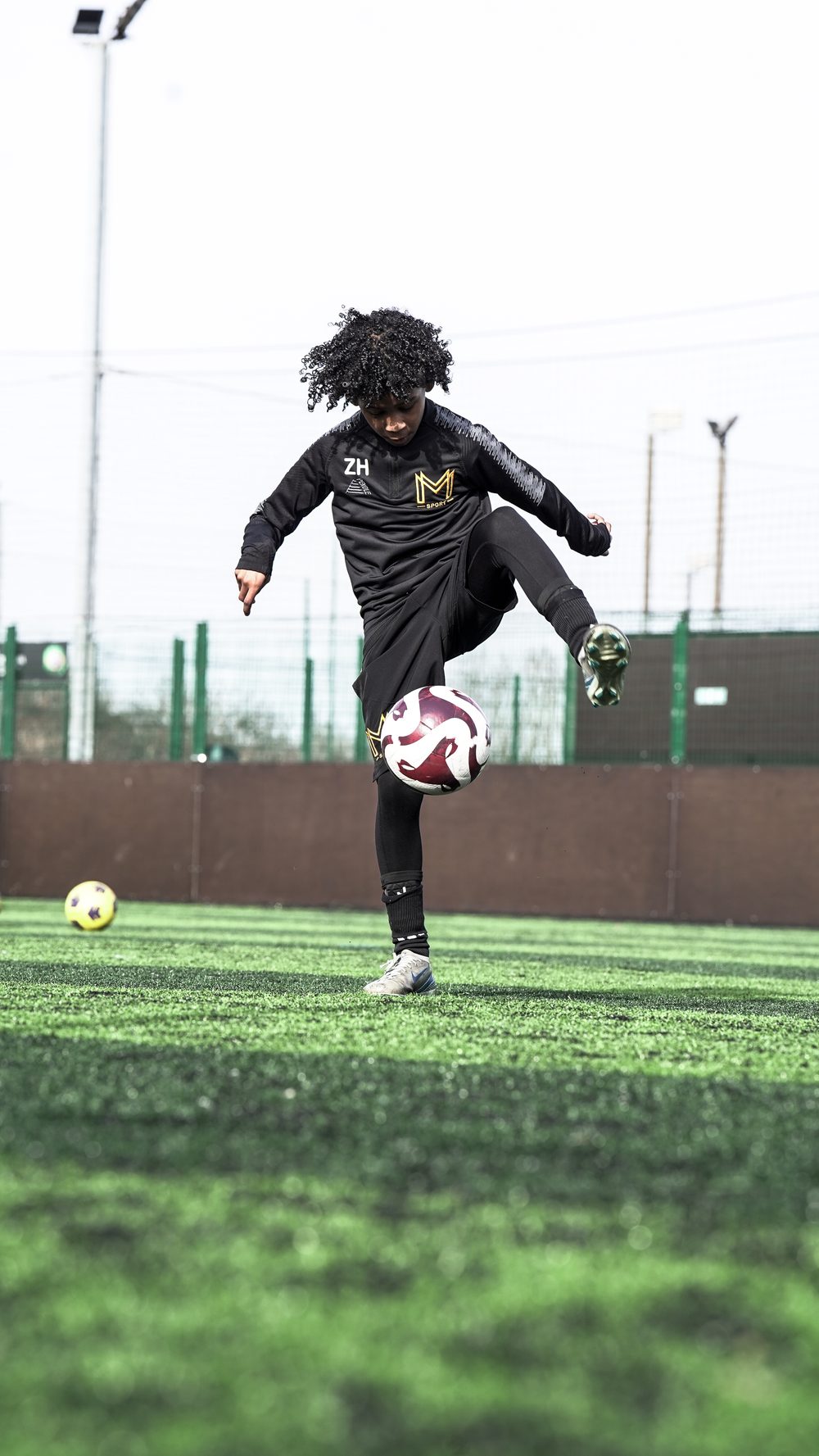 A young player in a black Monster Mentality Sport training top juggling a football with his knee on an artificial pitch