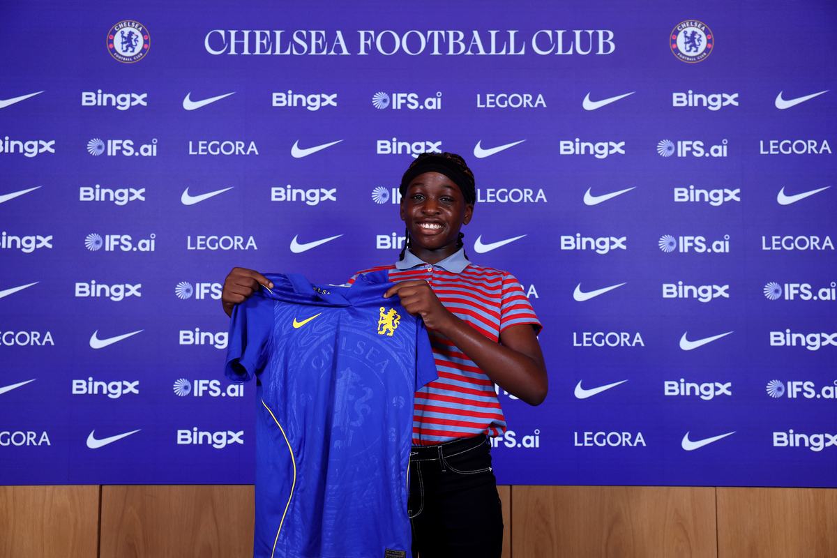 Smiling young player holding up a Chelsea shirt in front of the Chelsea Football Club backdrop