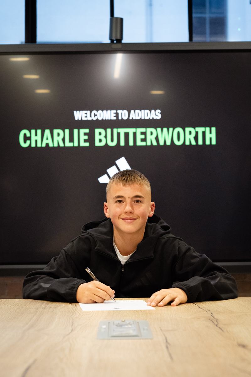 Young player signing at a table beneath a Welcome to adidas screen