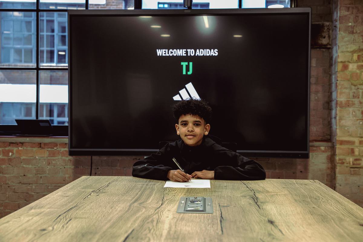 Young player signing at a long table beneath a Welcome to adidas screen