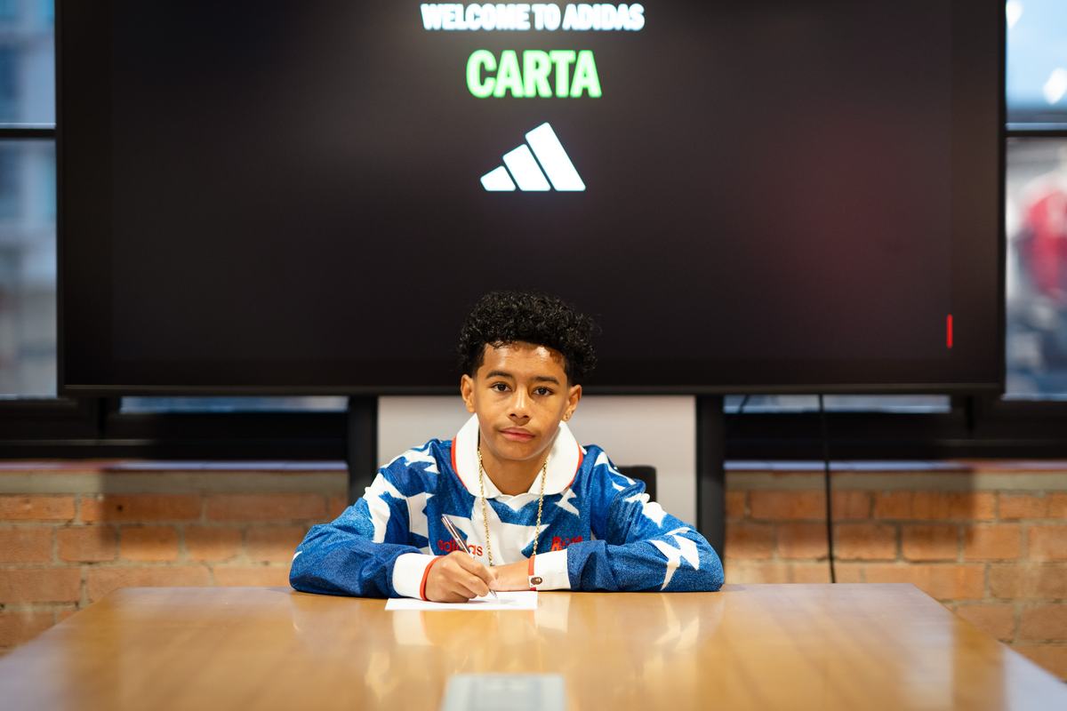 Young player signing at a table beneath a Welcome to adidas screen
