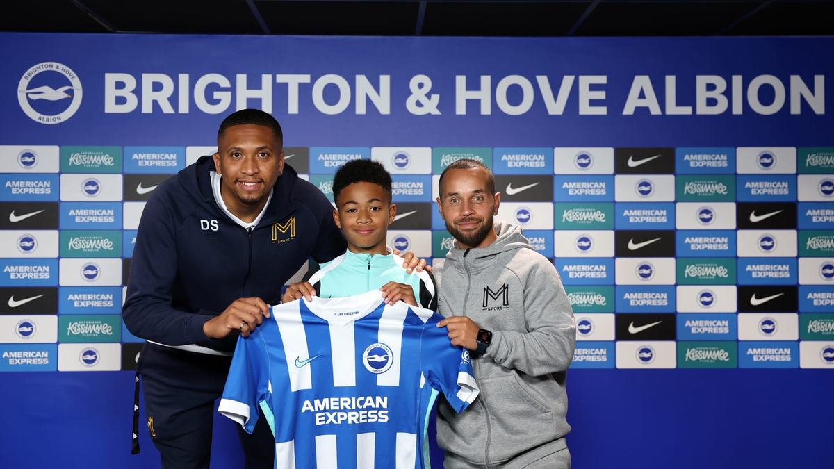 Young player holding a Brighton and Hove Albion shirt between two Monster Mentality coaches