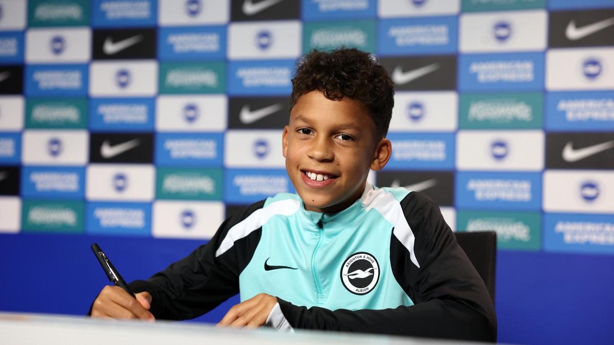 Smiling young player in a Brighton and Hove Albion training top, signing at a desk