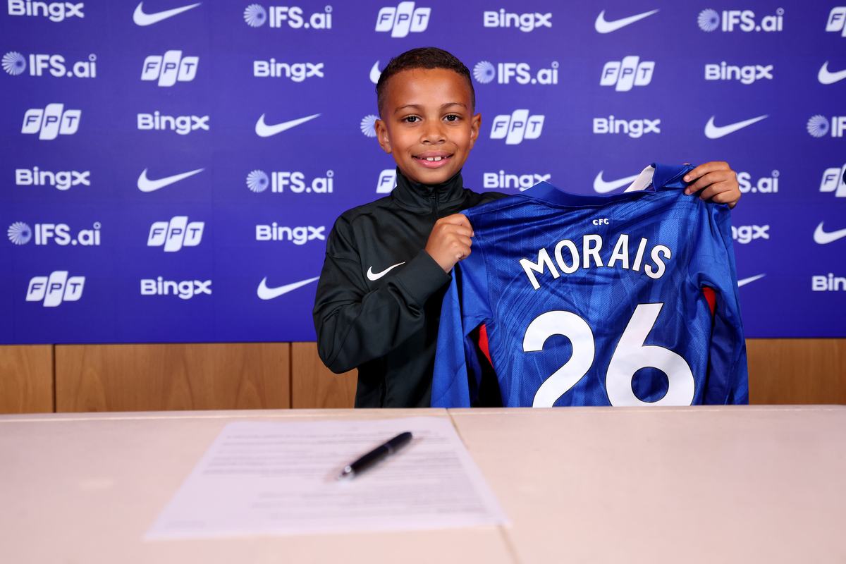 Smiling young player holding up a Chelsea shirt in front of the Chelsea Football Club backdrop