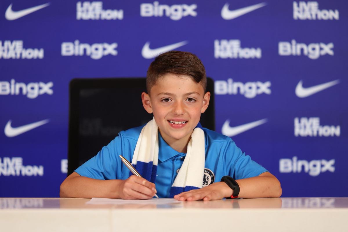 Smiling young player in a Chelsea polo and scarf, signing at a desk