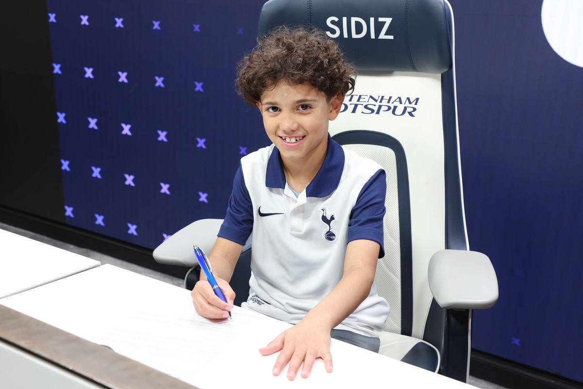 Smiling young player in a Tottenham Hotspur shirt signing in a Tottenham chair