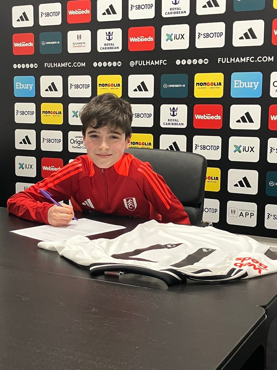Young player in a Fulham training top signing at a table with a Fulham shirt in front of him