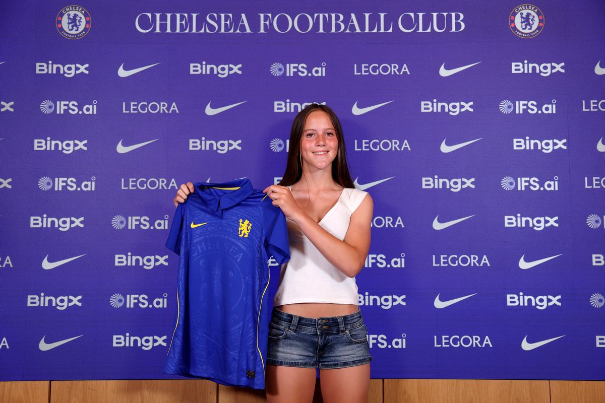 Young player holding up a Chelsea shirt in front of the Chelsea Football Club backdrop