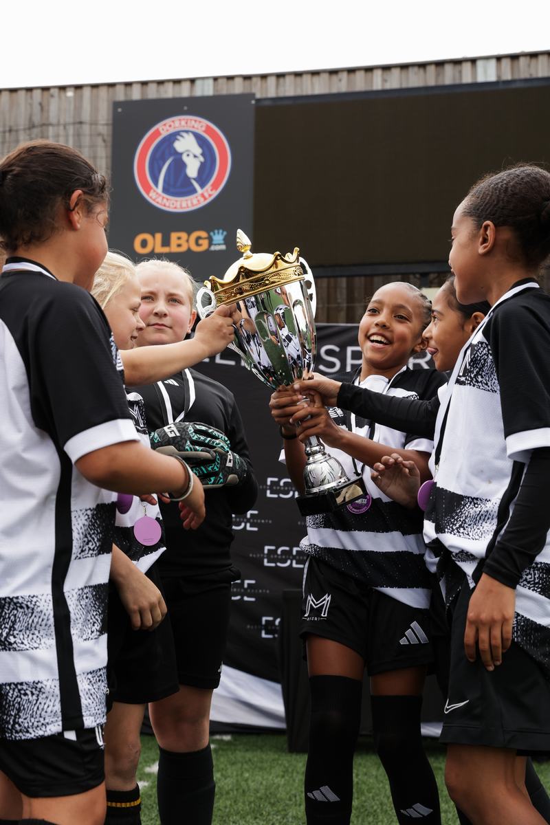 Girls in Monster Mentality Sport kit lifting a trophy together